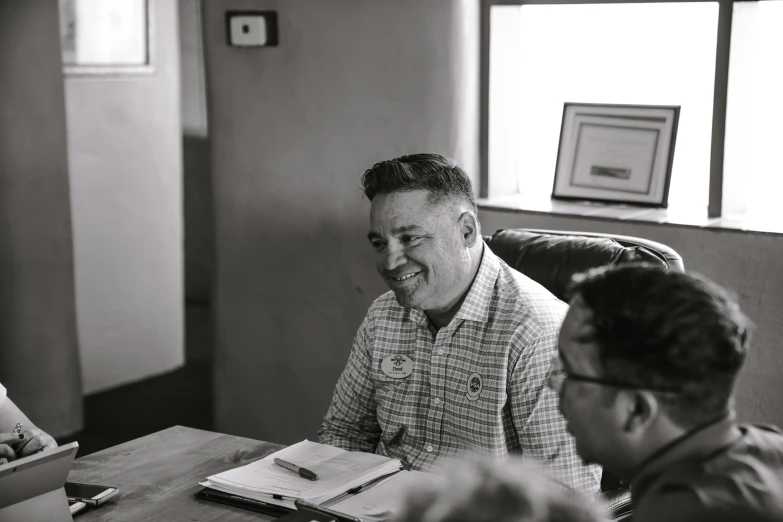 a man in plaid shirt sitting at table and talking to another person