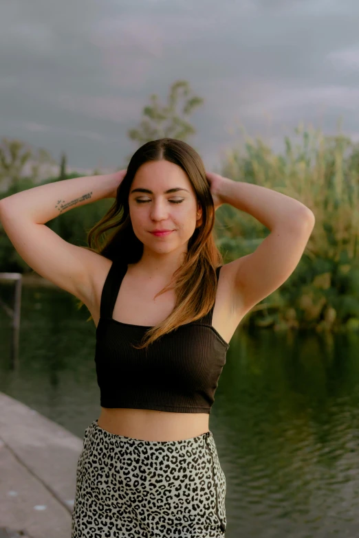 a girl wearing a leopard print skirt and a crop top stands against the riverbank