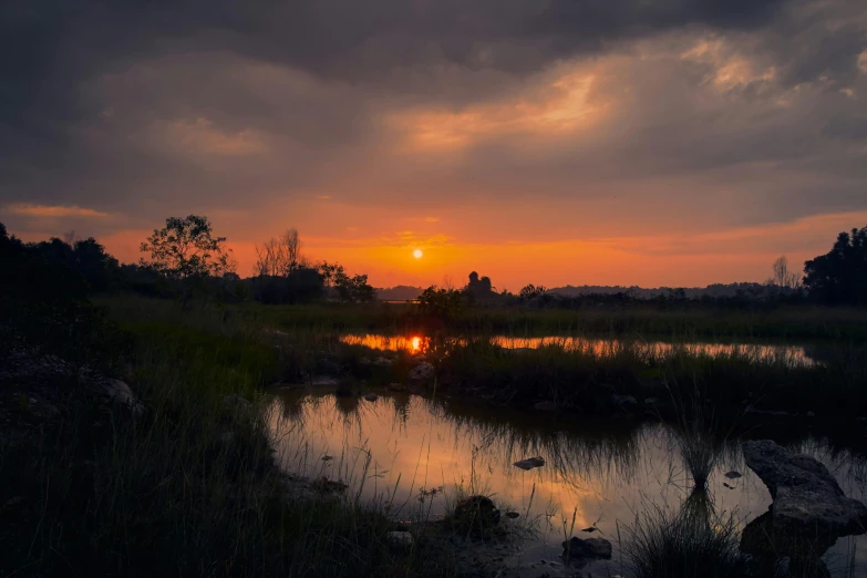 a sunset with the sun setting over a marsh