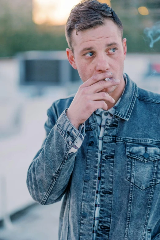 a man wearing a jean jacket smoking a cigarette