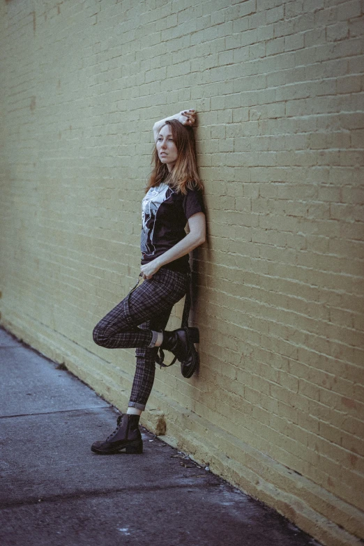 young woman leaning on a brick wall near a sidewalk