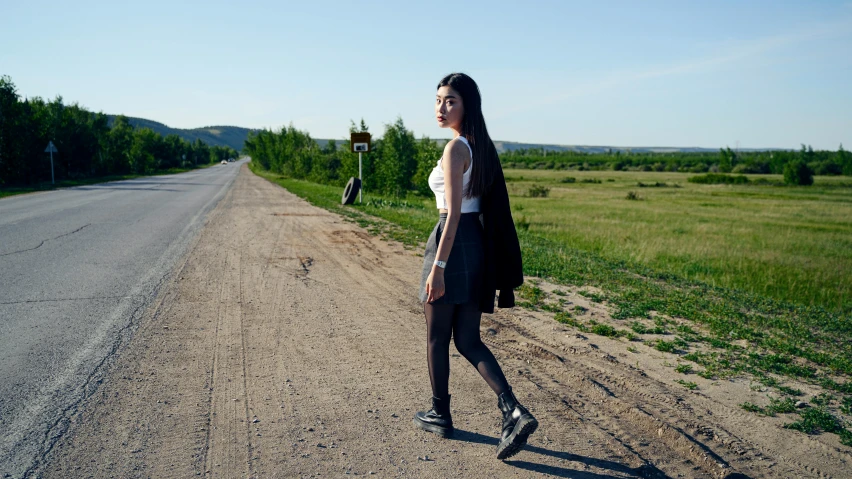 a woman on a dirt road next to a field and trees