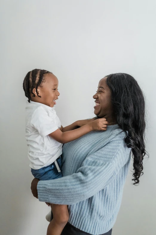 an african american woman is holding a small child and she is wearing a blue sweater