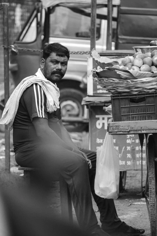 an old picture of a man sitting at an outdoor stand selling fruit