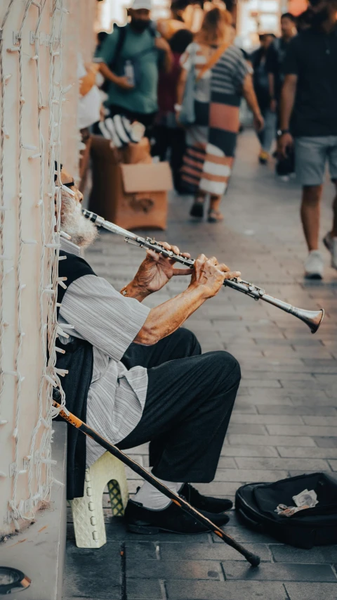 a man sitting on the sidewalk playing a flute