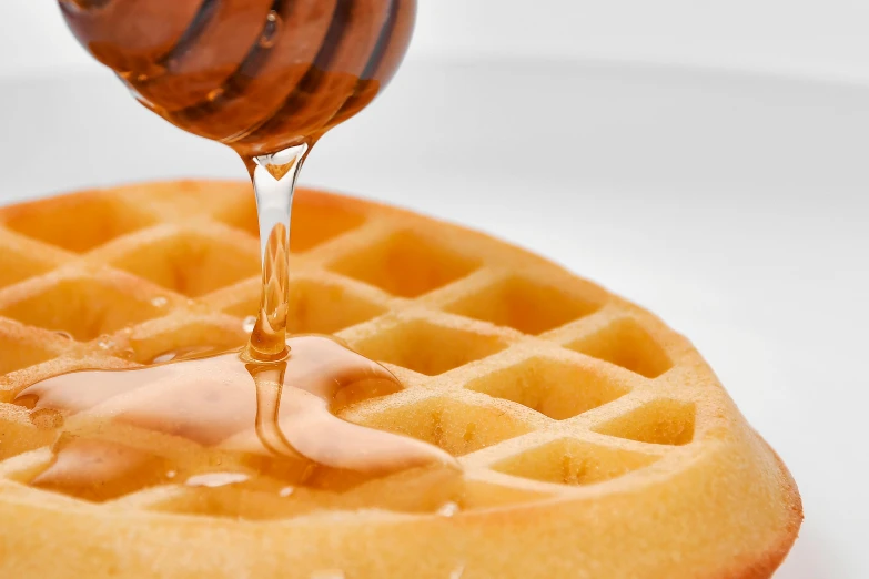 a bee dips honey from a waffle on a plate