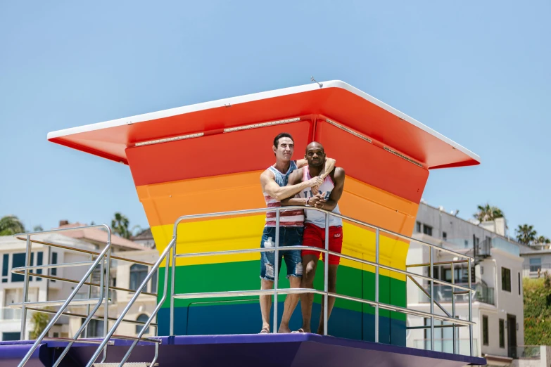 two men standing on the side of a boat near a rainbow colored structure