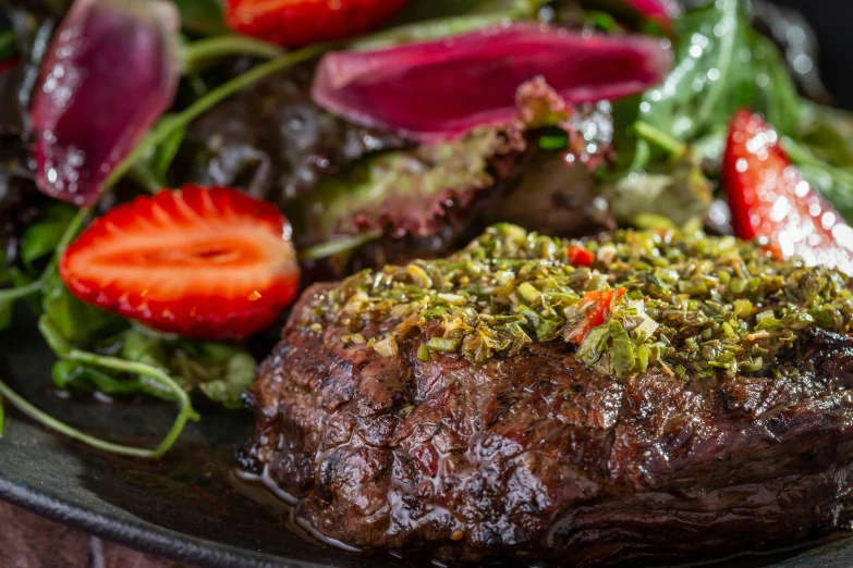 steak, salad and strawberries are on a black plate