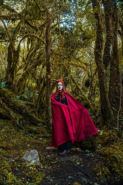 man with red cape standing in the forest