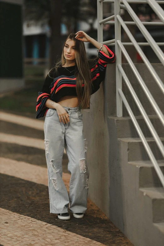 a girl leaning against a wall wearing jeans