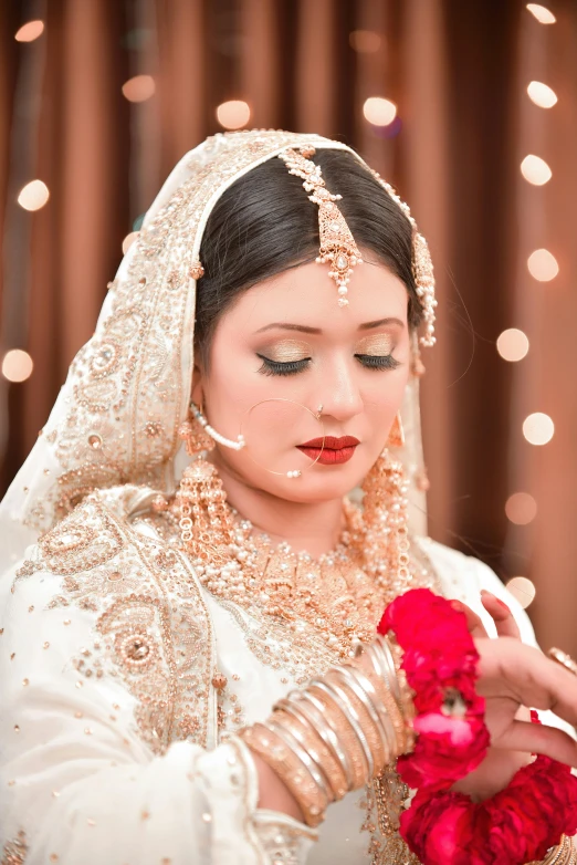 a bride holding a red flower, dressed in gold and white