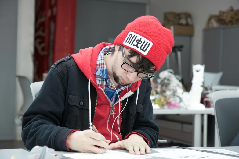 a man wearing a red hat writing in front of a computer