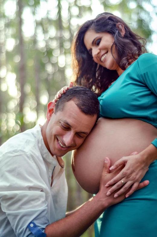 a smiling pregnant man poses with his stomach in a park