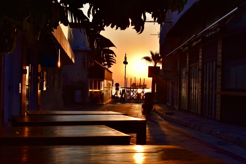 a sun setting on the side of a street with benches on both sides