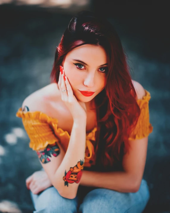 a young woman with red hair and tattoo sitting on the ground