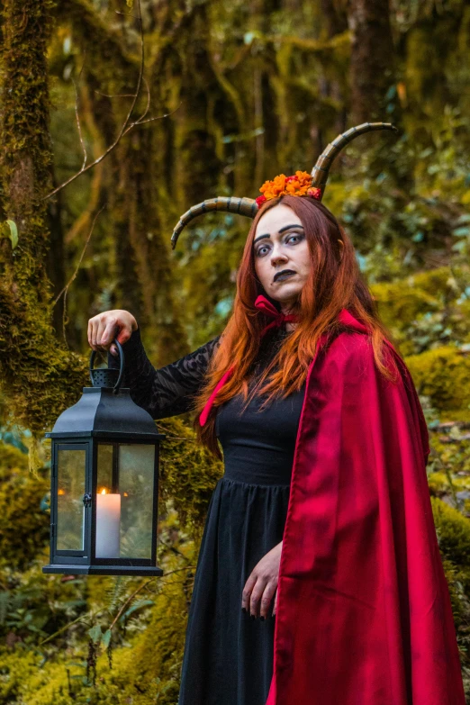 a young woman dressed in costume holds up an old fashioned lantern in the woods