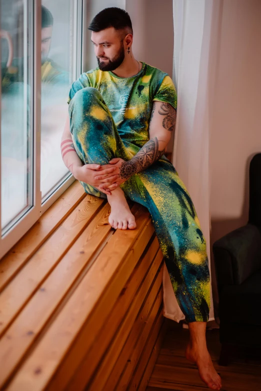 a man in an artful tie - dyed outfit sits on a window sill