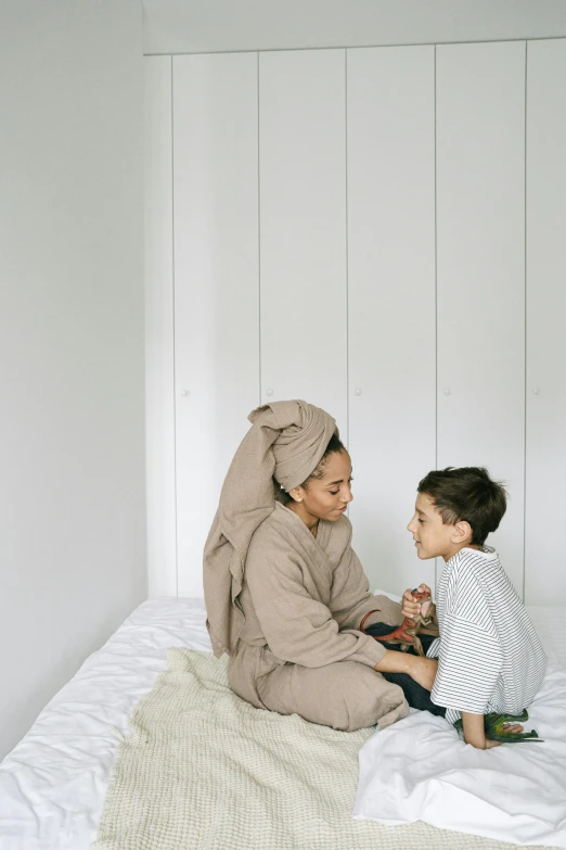 a woman sitting on top of a bed next to a little boy