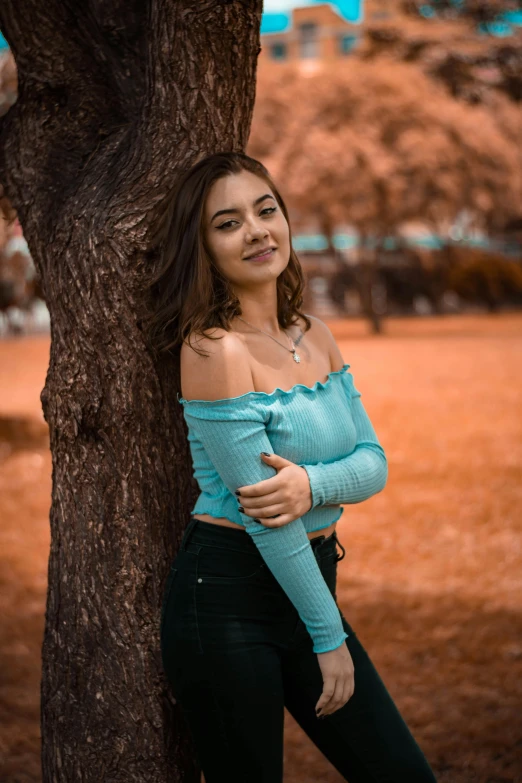 a beautiful young woman standing next to a tree