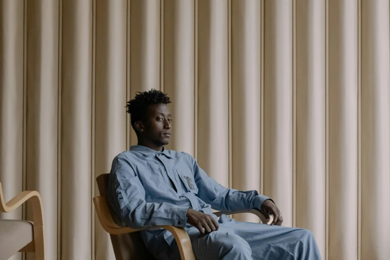 a man in blue shirt sitting on chair next to window