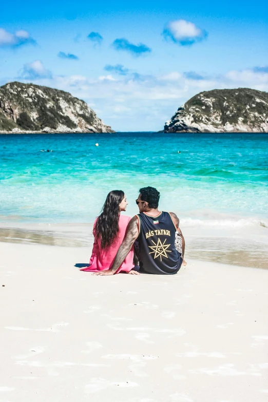 two people sitting in the sand on a beach