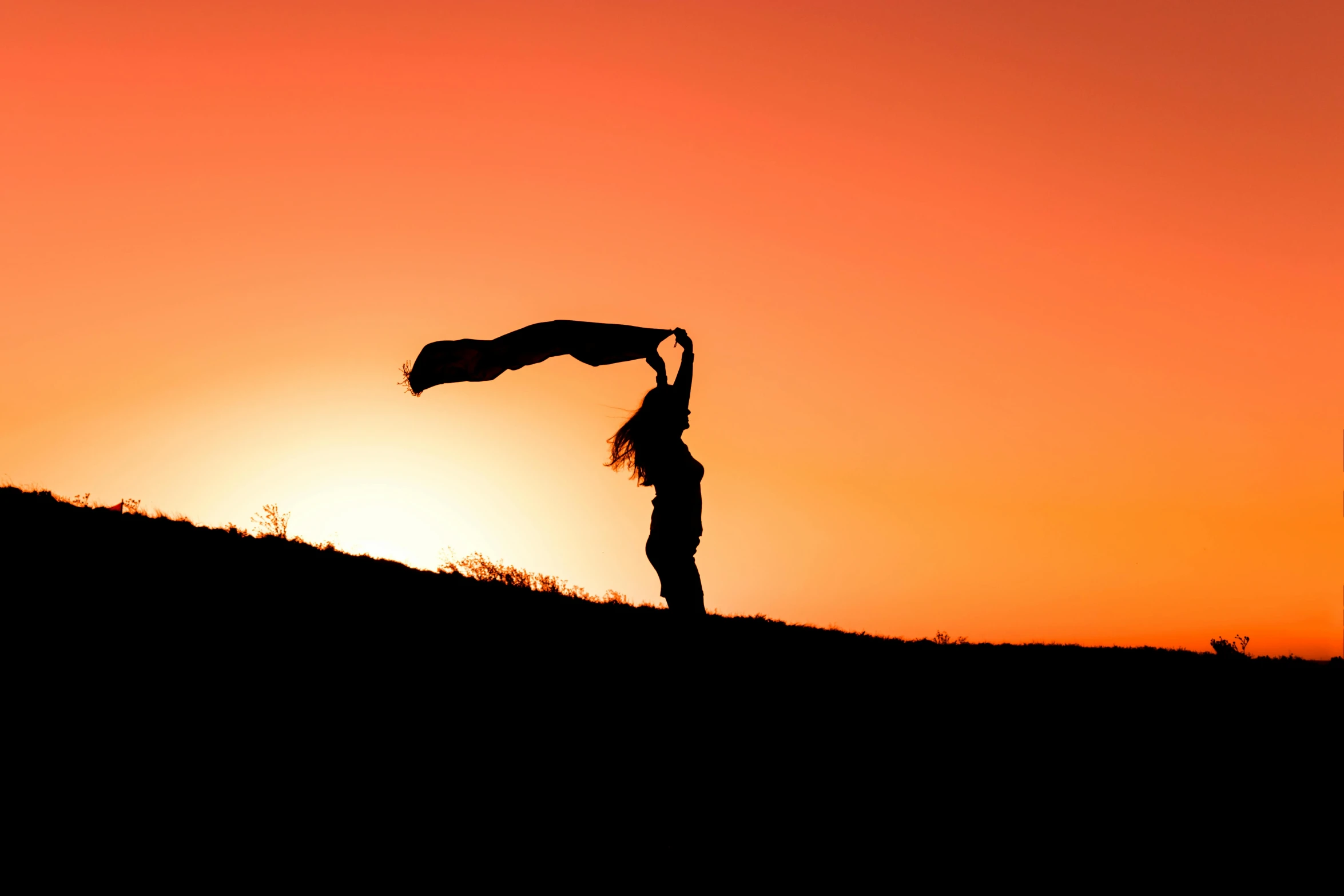 a person standing on a hill holding a scarf over their head at sunset