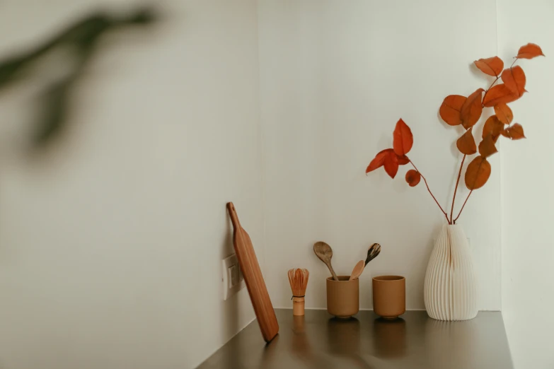 a white wall with a vase, spoons and cup with leaves