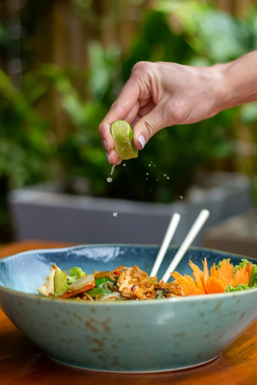 someone sprinkles green leaves over a colorful bowl