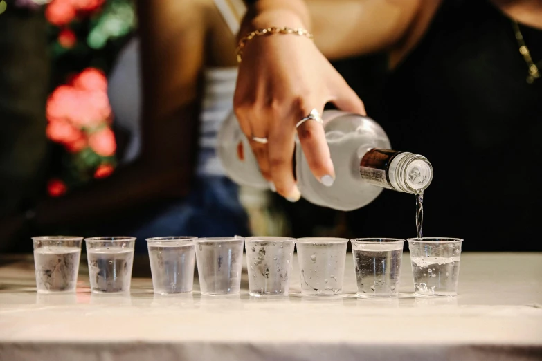 a person is pouring water into a row of glasses