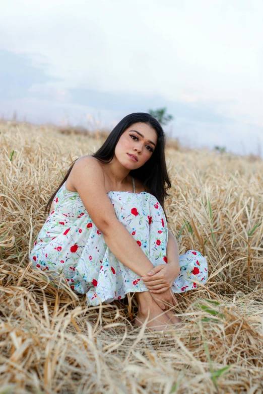 a woman is sitting on the ground next to dry grass