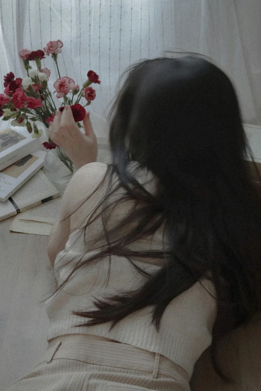 a girl on the floor with her head turned to the side, holding flowers in one hand and reading a book beside her