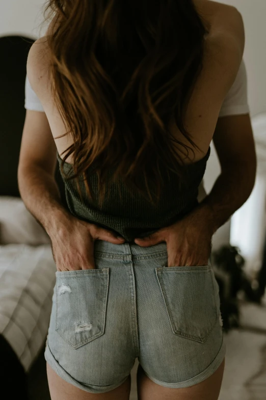 a girl wearing shorts with no pants on, is standing in front of a bed