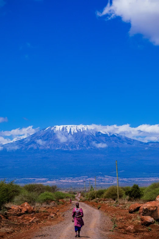 a woman walking on a dirt road with snow covered mountains in the background