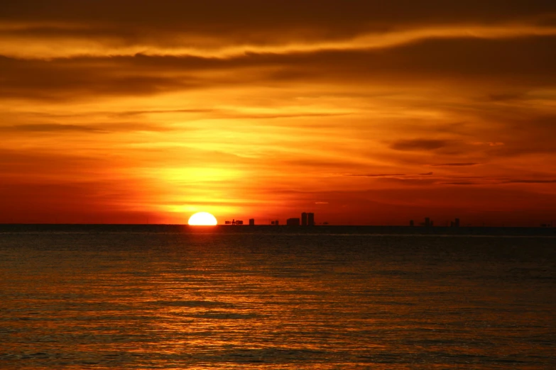 the sun is setting in an orange sky above a calm sea