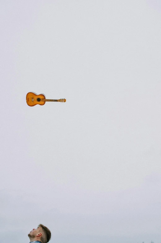 a man on a field flying a kite with an orange guitar attached to it