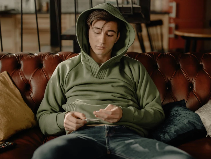 a man in green sweatshirt sitting on brown couch
