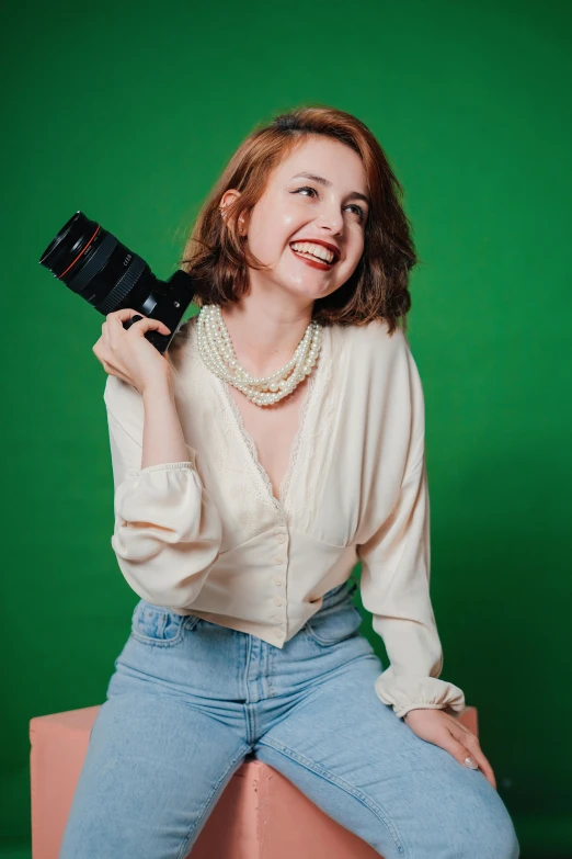 a woman is posing with her camera in front of a green background