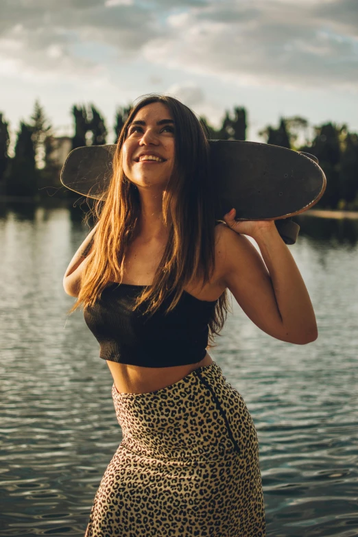 a woman in leopard print skirt and crop top holds a skateboard over her head