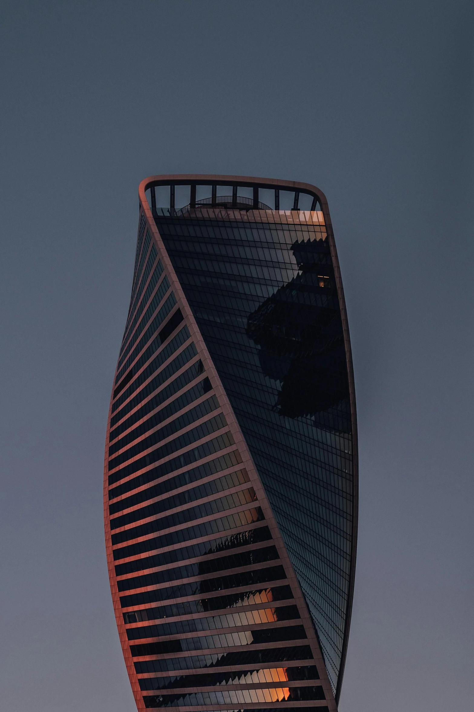 the tall tower has a curved edge and dark blue sky