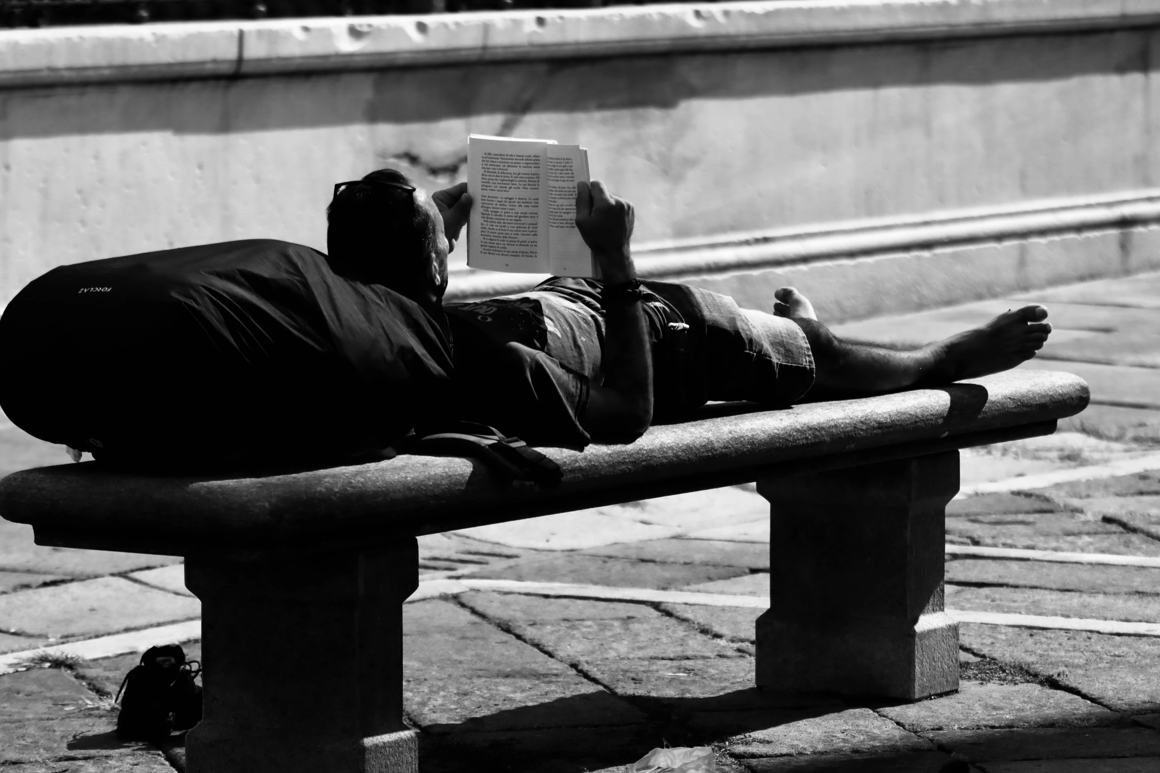 the man is reading a book while lying on a bench