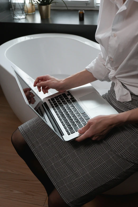 a person sitting in front of a bathtub holding a laptop