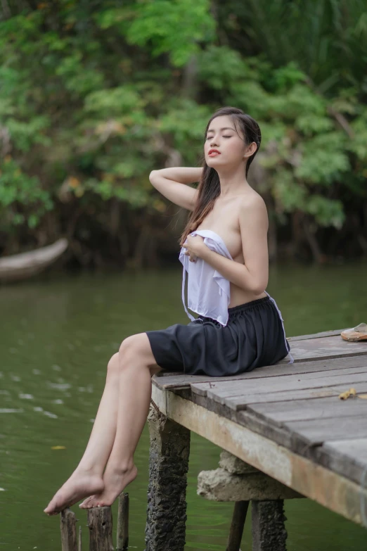 woman in white top sitting on dock next to body of water
