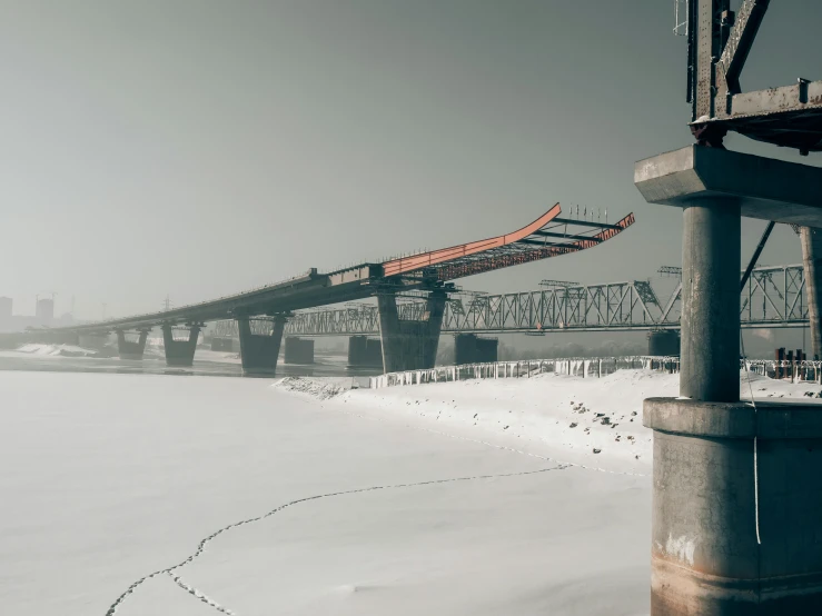 an empty, snowy field that has a large bridge in the background