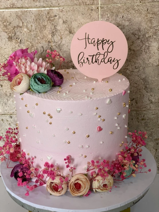 a pink birthday cake with flowers and pearls on the front