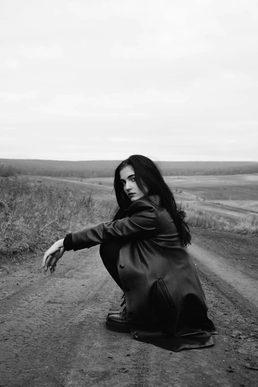 the woman is kneeling on the dirt road near a sign