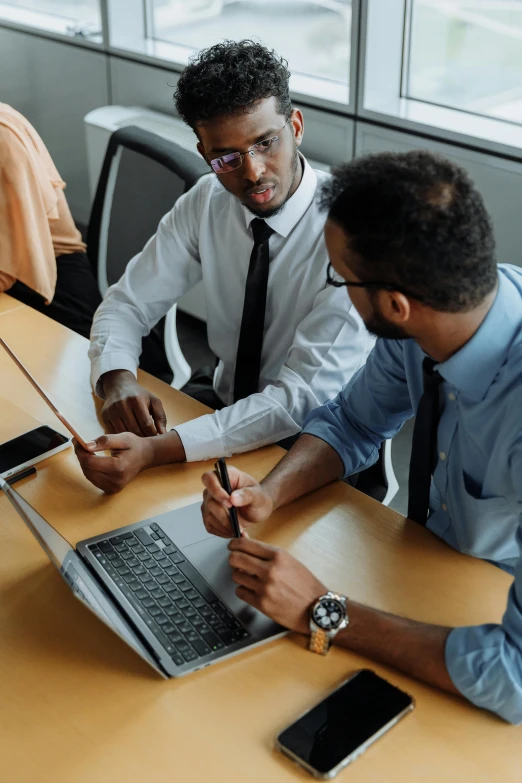 a pair of men sitting at a desk working on their laptops