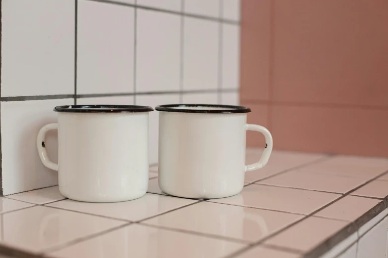 two coffee mugs sit on the counter, with tile in the background