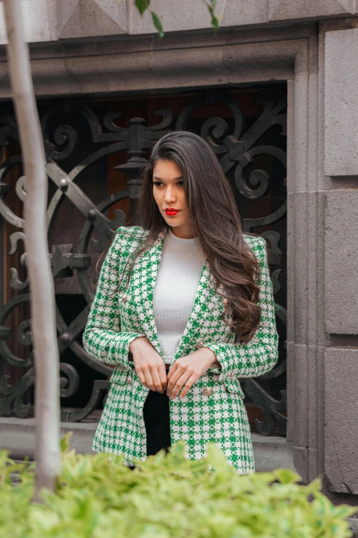 a woman with long dark hair and red lipstick dressed in a green coat, looking down