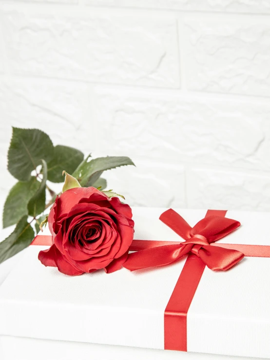 a red rose with a red ribbon sits on a white present box