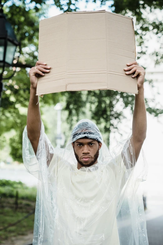 a man holds up a cardboard sign in front of his head